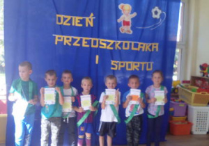 Grupka dzieci w zielonych szarfach pozująca do zdjęcia trzymająca przed sobą dyplomy.