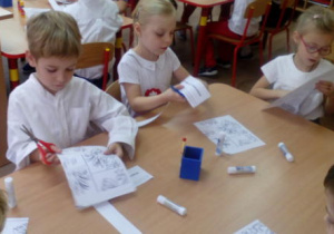 Troje dzieci przy stoliku rozcina puzzle "Godło" do ułożenia.