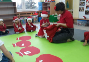 Nauczycielka siedzi na macie z workiem Mikołaja, dzieci siedzą dookoła niej