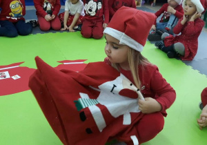 Dziewczynka wyjmuje kartkę z ilustracja z worka Świętego Mikołaja