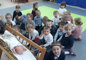 Dzieci siedzą przy żłóbku z dzieciątkiem Jezus