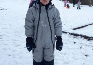 Chłopiec ubrany w kombinezon stoi na sniegu