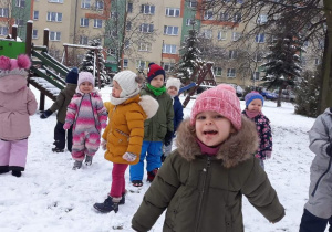Dzieci stoją na śniegu w ogrodzie przedszkolnym