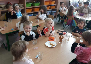 Dzieci siedzą przy stołach, jedzą ciasteczka