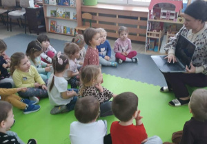 Dzieci patrzą w stronę nauczycielki, która pokazuje im komputer