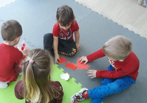 Na zdjęciu widocznych jest czworo dzieci, które układają puzzle