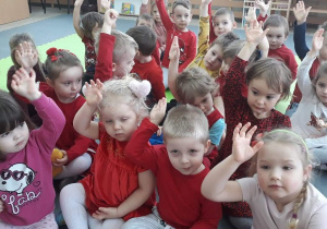 Dzieci trzymają dłonie w górze zgłaszając się do odpowiedzi przy tablicy
