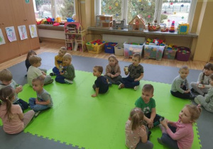 Dzieci siedzą na macie w pięciu grupach. Jedno dziecko z każdej grupy trzyma słoiczek ze śmietaną.