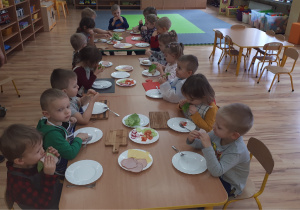 Przedszkolaki przy stolikach jedzą przygotowane przez siebie kolorowe kanapki.