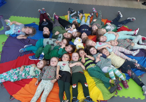 Grupa dzieci leży na plecach na kolorowej chuście animacyjnej
