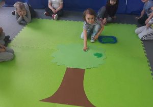 Dziewczynka trzyma dłoń zamoczoną w zielonej farbie na papierowym drzewie