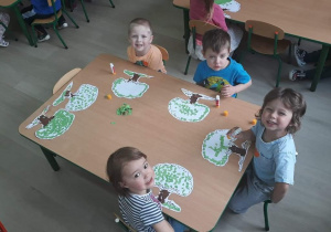 Dzieci pozują do zdjęcia przy stoliku, uśmiechają się