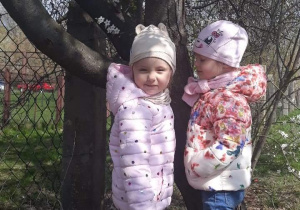 Dwie dziewczynki stoją przy wiosennym drzewie