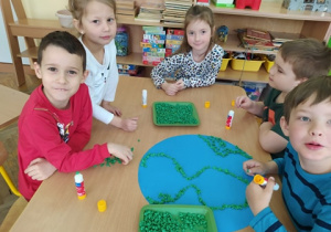 Dzieci wyklejają szablon Ziemi zielonymi kulkami z bibuły.
