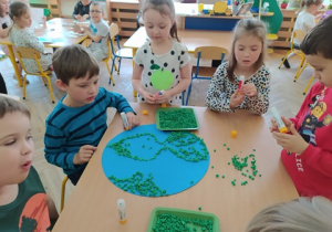 Dzieci wyklejają szablon Ziemi zielonymi kulkami z bibuły.
