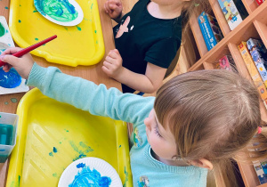 Wiktoria i Milenka malują Ziemię używając niebieskiej i zielonej farby.