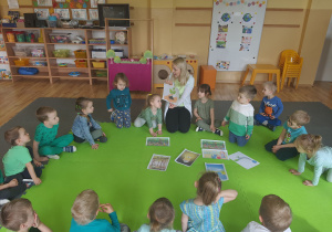 Grupa dzieci siedzi w kole, nauczycielka pokazuje ilustrację odnoszącą się do sadzenia drzew.