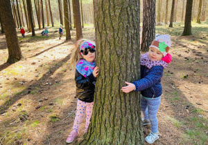 Wiktorka i Milenka przytulają się do drzewa.