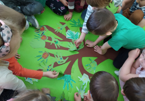 Dzieci wspólnie tworzą prace plastyczną przedstawiającą duże drzewo.