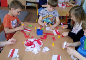 Dzieci siedzące przy stoliku podczas wykonywania flagi na patyczku.