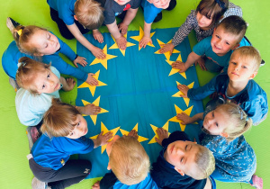 Grupa dzieci trzyma ręce na samodzielnie utworzonej fladze Unii Europejskiej.