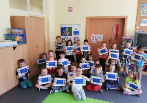 Grupa dzieci pozuje do zdjęcia z Flagą Unii Europejskiej słuchając hymnu Unii Europejskiej