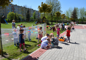 Pięknie świeci słońe, widom na trzy grupy dzieci malujących na foli, w tle przedszolny plac zabaw