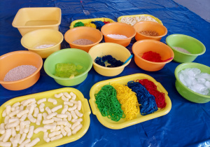 Kolorowe miski i tace, a w nich kolorowy makaron, galaretki, chrupki kukurydziane, lód, ryż.
