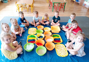 Dzieci siedzą wokół kolorowych produktów spożywczych.