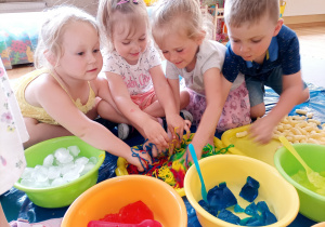 Dzieci manipulują kolorowo wybarwionym makaronem.