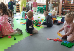 Dzieci siedzą na macie piankowej, bawią się