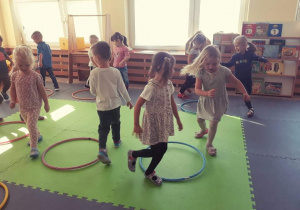 Dzieci biegają przy obręczach, na sygnał nauczyciela wskakują do środka obręczy