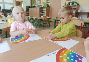 Dziewczynka i chłopiec wyklejają kropki kolorową plasteliną.