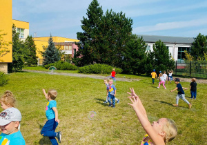 Przedszkolaki biegają po ogrodzie łapiąc mydlane bańki.