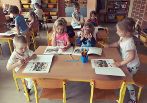 Dzieci siedzą przy stolikach- pracują w podręcznikach