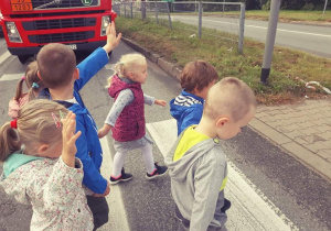 Dzieci z podniesioną ręką przechodzą na druga stronę jezdni