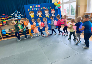 Przedszkolaki tworzą pociąg z kolorowymi balonami i tańczą do piosenki "Jedzie pociąg z daleka".