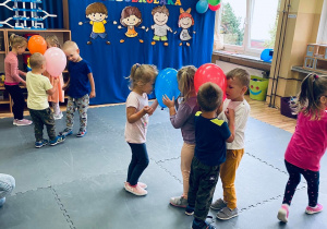 Przedszkolaki tańczą w parach trzymając kolorowe balony pomiędzy główkami.