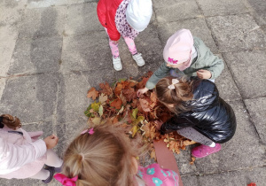 Dziewczynki układają koronę drzewa z liści.