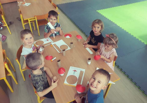 Dzieci siedzą przy stoliku kleja muchomorka według podanej instrukcji