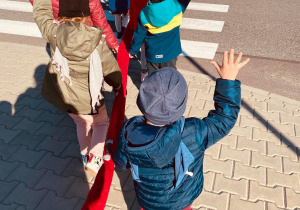 Dzieci przechodzą przez ulicę podnosząc rączki do góry.