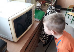 Chłopiec obserwuje podgrzewany obrazek dyni w kuchence mikrofalowej