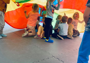 Roześmiane dzieci pozują pod kolorową chustą.