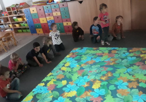 Grupa dzieci zgromadzona wokół wyświetlającego się obrazu jesiennych liści.