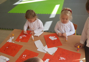 Dzieci naklejaja na sylwete orła wydzieranke z bialego papieru