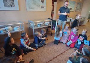 Dzieci siedzą w kole i słuchają opowieści przewodnika muzeum