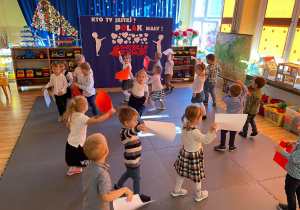 Dzieci tańczą machając biało-czerwonymi kartkami.