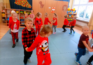 Ubrane na czerwono przedszkolaki ustawione są jedno za drugim w parach, uczestnicząc w zabawie.