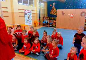 Przedszkolaki ubrane na czerwono siedzą na macie.