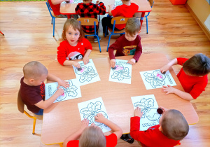 Dzieci w czerwonych ubrankach malują burakiem kontur buraczka.